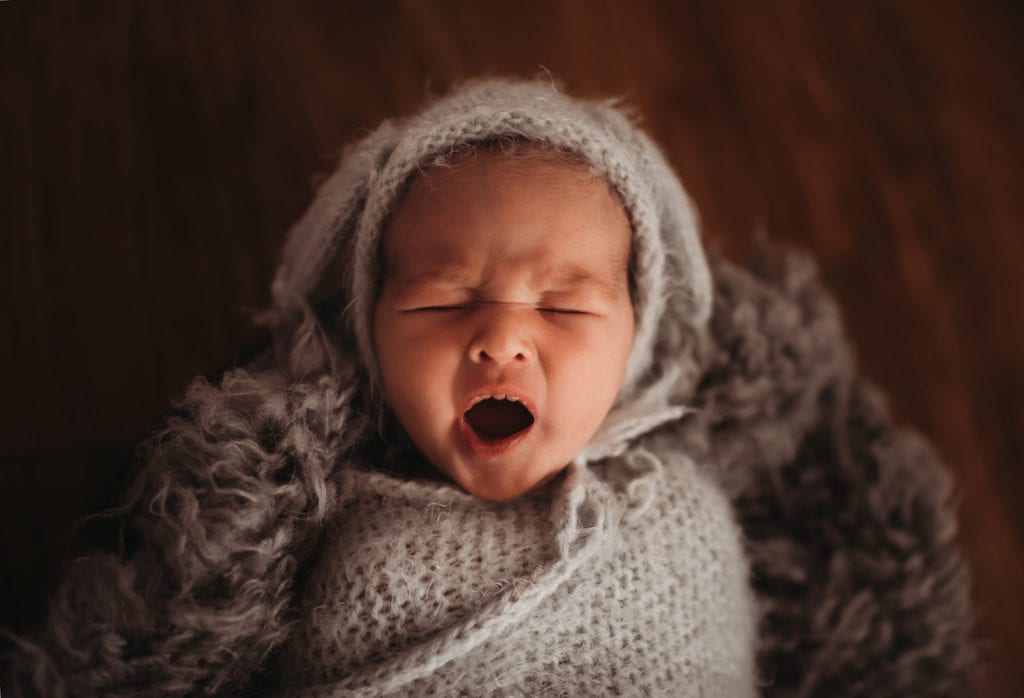 Newborn Photographer, a baby yawns while bundled in blankets atop a basket
