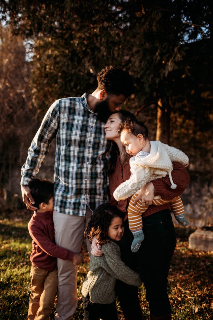Family Photographer, Mom and Dad lean into each other with their three children beside them at the park