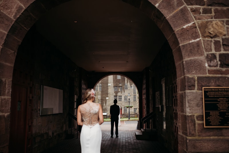 Wedding Photographer, a bride in her dress approaches her groom from behind in a park tunnel
