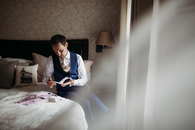 Wedding Photographer, a groom sits on the bed reading a wedding card