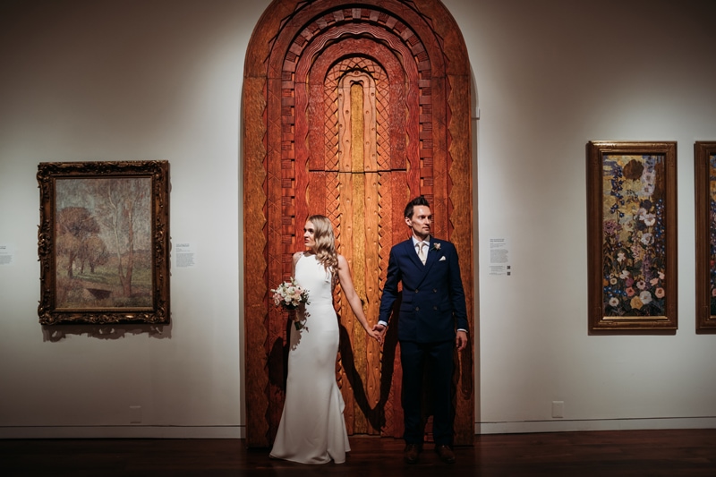 Wedding Photographer, a bride and groom hold hands in front of an ornately patterned door at the museum