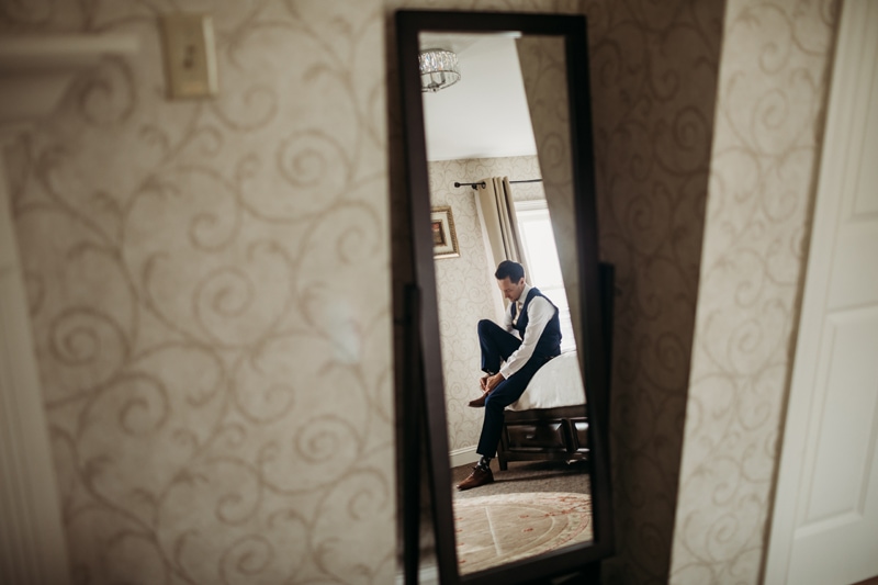 Wedding Photographer, a groom is in a mirrors reflection putting on his shoes for the big day
