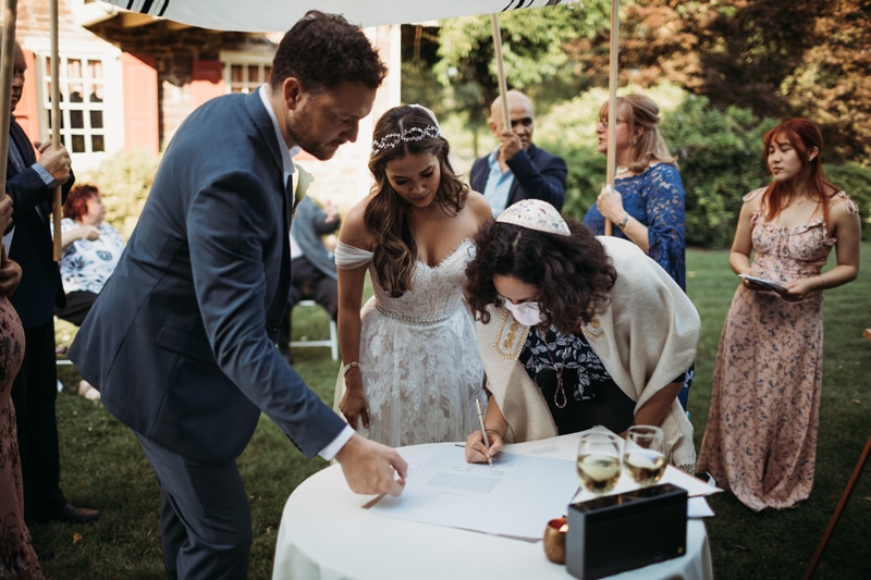 Wedding Photographer, the wedding officiant signs wedding papers beside bride and groom