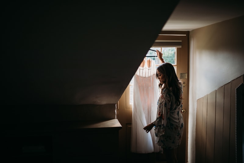 Wedding Photographer, woman holds a wedding dress up at home