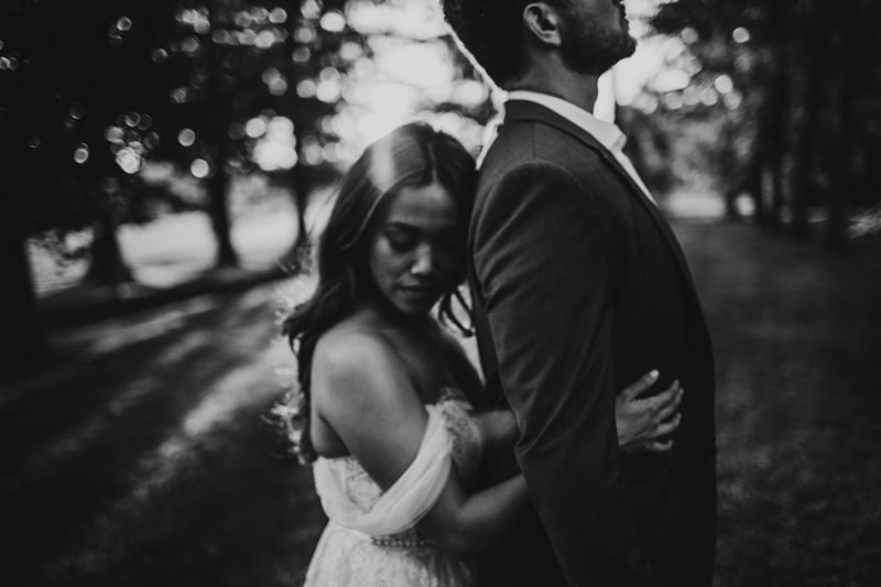 Wedding Photographer, bride holds her husband from behind under the trees at a park