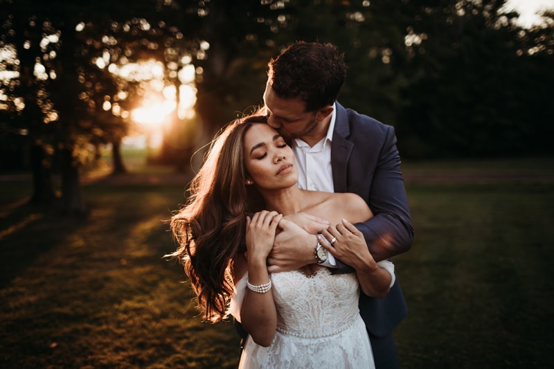 Wedding Photographer, man kisses his newly married wife on the forehead in the park