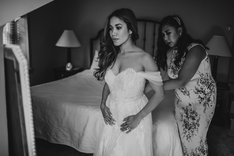 Wedding Photographer, a bridesmaid helps the bride with her wedding dress