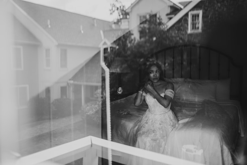 Wedding Photographer, a woman stands in a window with her wedding dress on