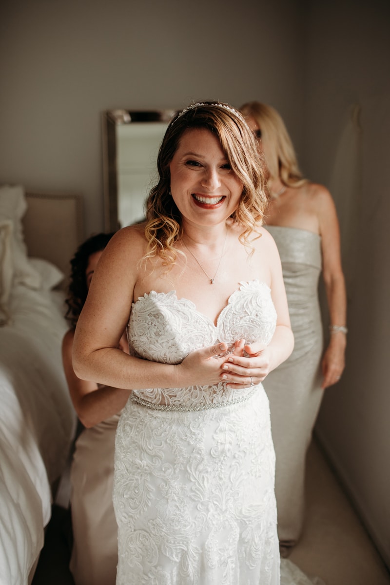 Wedding Photographer, a bride smiles, her bridesmaid help her get ready