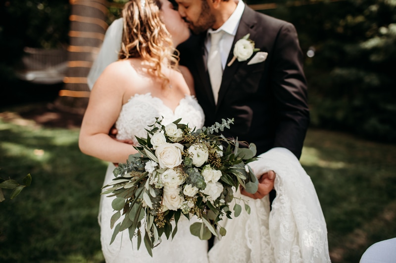 Wedding Photographer, a bride and groom kiss outside, she holds her large bouquet of flowers