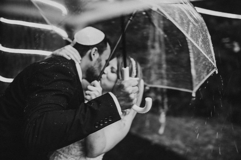 Wedding Photographer, bride and groom kiss under an umbrella in the rain