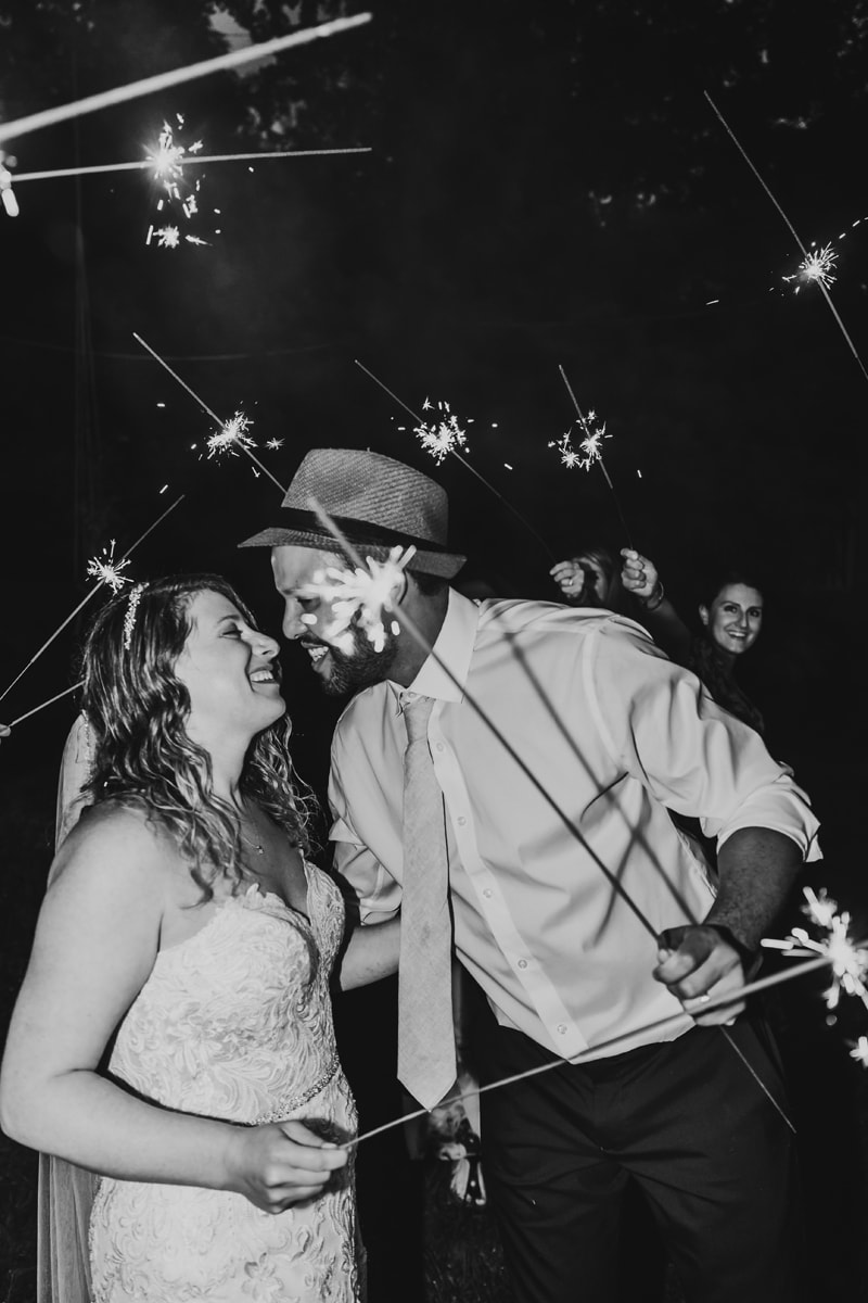Wedding Photographer, bride and groom lean in for a kiss amidst a crowd holding sparklers