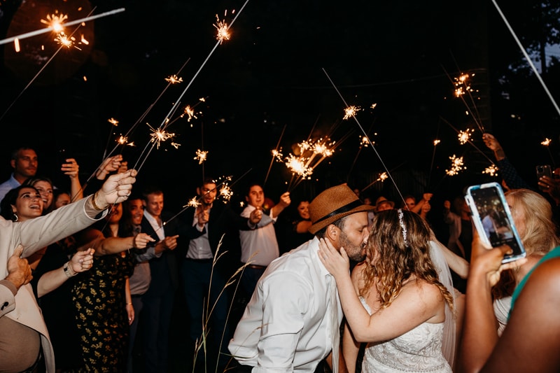 Wedding Photographer, bride and groom kiss under a ceiling of sparklers held by friends and family