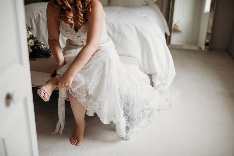 Wedding Photographer, a woman puts on her shoes for her wedding at her bedside