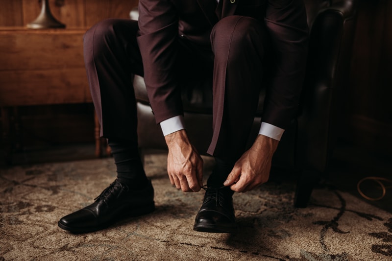 Wedding Photographer, a groom in suite ties his shoes