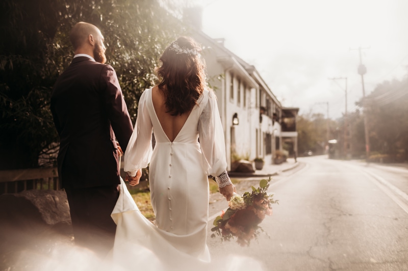 Wedding Photographer, bride and groom walk hand in hand down a village street