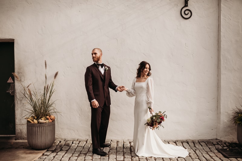 Wedding Photographer, bride and groom stand together in their gown and suit on cobblestones