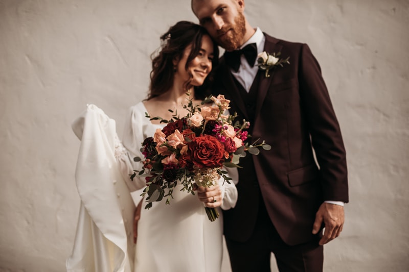 Wedding Photographer, a bride and groom lean into each other tenderly, she holds her bouquet of flowers